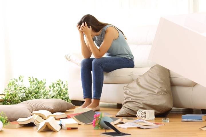 Desperate homeowner complaining after home robbery sitting on a couch of the messy living room at home